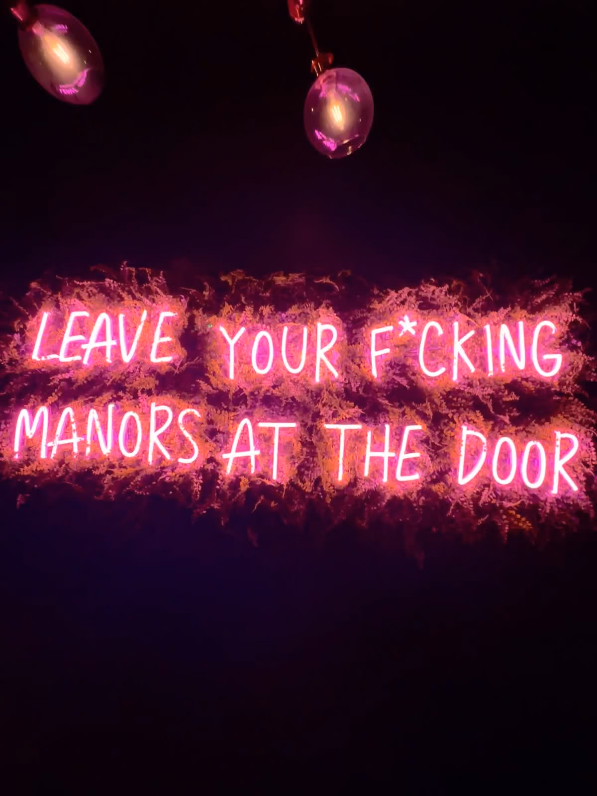 Pink neon sign at NO Manors reading “Leave your f*cking manors at the door.”